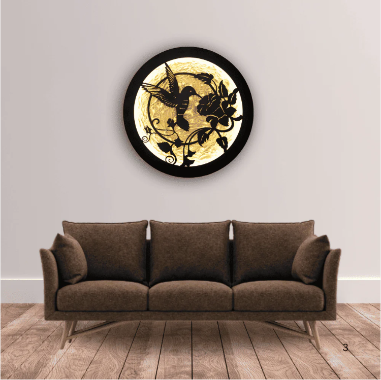 Round LED wall art featuring a laser-cut hummingbird and floral design, backlit with warm neon lighting, mounted on a white wall in a minimalist room.