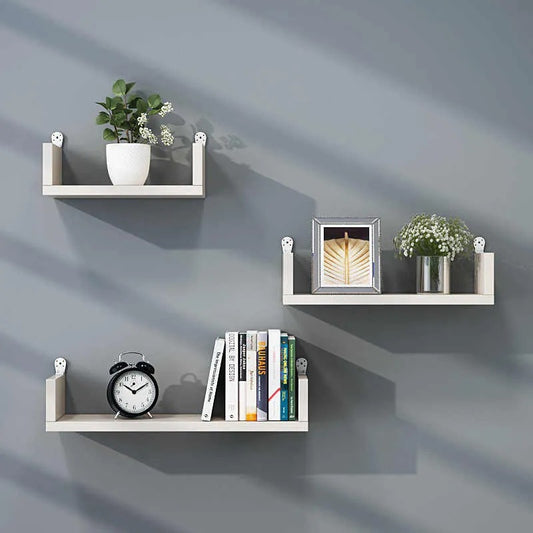 "Set of three minimalist floating wall shelves on a grey wall with books, plants, and decor items."