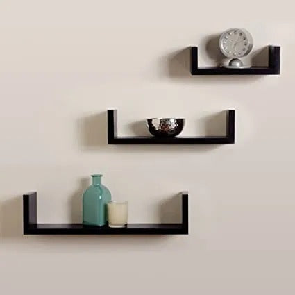 "Set of three minimalist floating wall shelves on a grey wall with books, plants, and decor items."