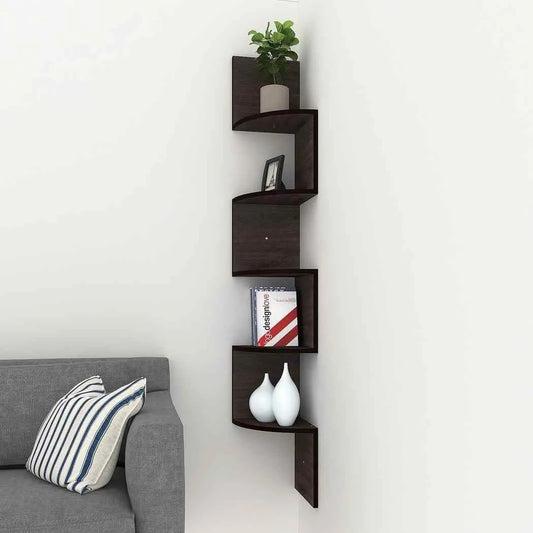 "Dark wooden zigzag corner wall shelf mounted beside a grey sofa, holding decor, books, and a plant."