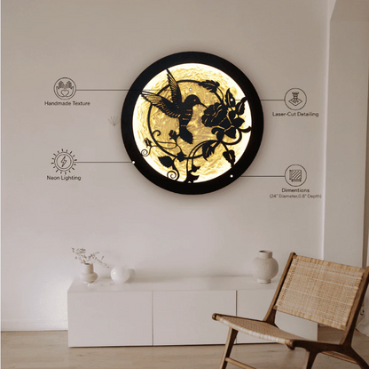 Round LED wall art featuring a laser-cut hummingbird and floral design, backlit with warm neon lighting, mounted on a white wall in a minimalist room.


