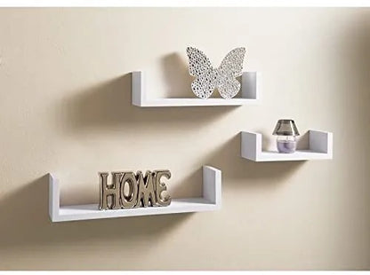 "Set of three minimalist floating wall shelves on a grey wall with books, plants, and decor items."