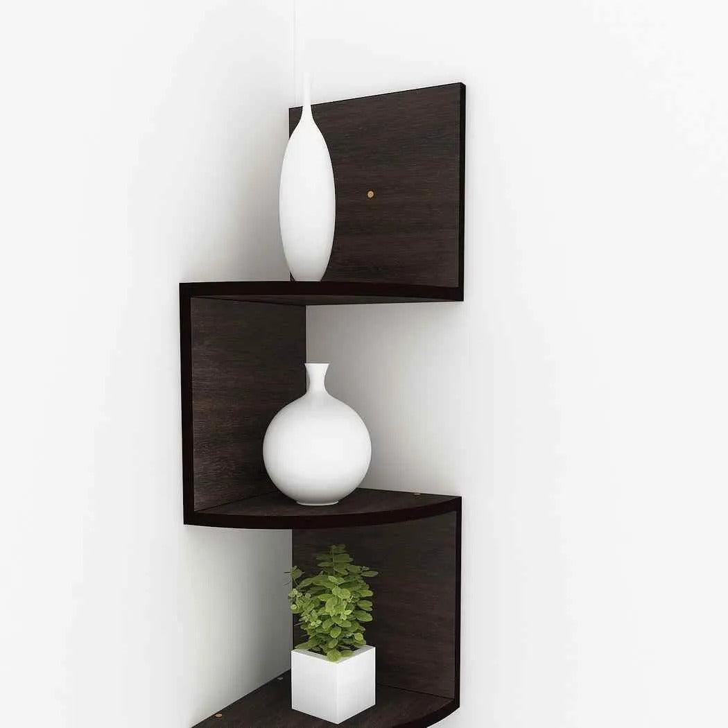 "Dark wooden zigzag corner wall shelf mounted beside a grey sofa, holding decor, books, and a plant."